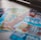 A selection of colorful lottery scratch-off tickets placed on a flat surface near a window. The image has a shallow depth of field, focusing on the tickets while blurring the background. The tickets display various games and prize amounts.