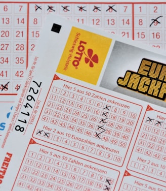 Three lottery tickets are displayed, including Eurojackpot and Super 6. Various numbers are marked on the tickets, with some crossed out and others checked. The Eurojackpot ticket is partially visible with the logo prominently displayed, and a ticket number is visible on one of the tickets.