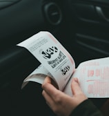 A person is holding and examining what appears to be lottery tickets inside a car. The image is focused on the tickets and the person's hands, with parts of the car interior visible in the background.