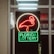 A neon sign depicting a flamingo above the words 'Florida Lottery' is prominently displayed. The sign is illuminated in bright red and green colors, and it is framed by glass panels. An 'EXIT' sign is visible in the background.